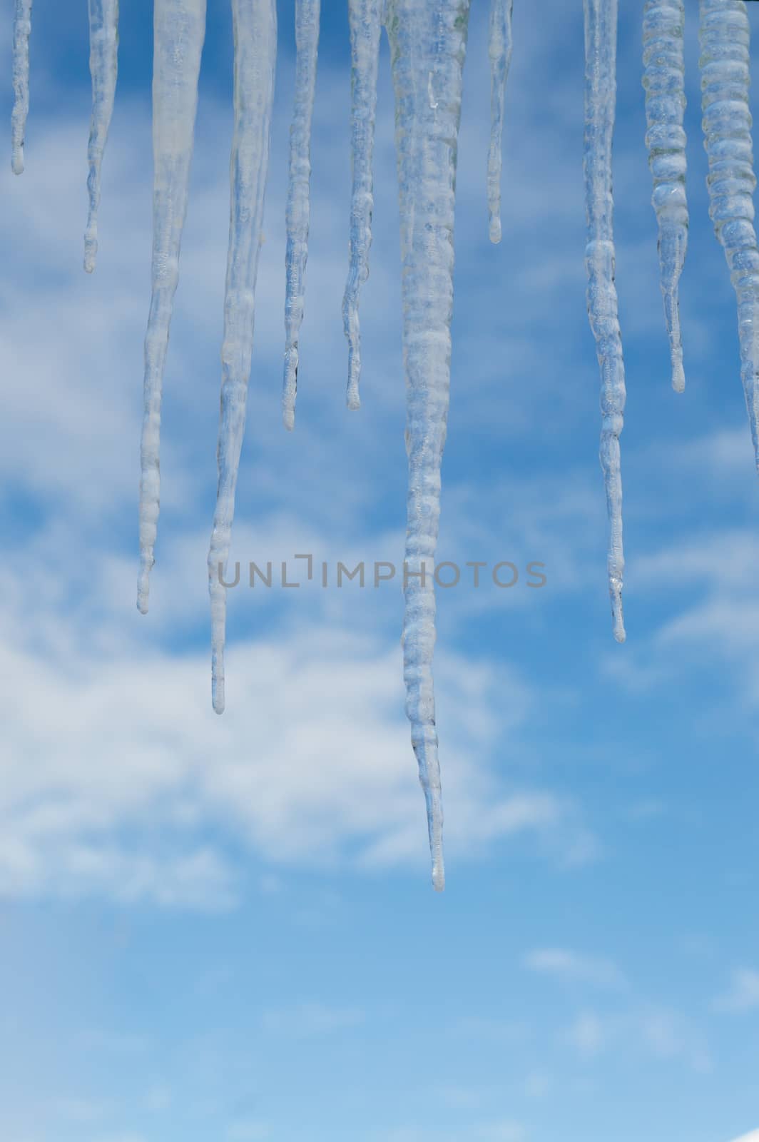 Closeup of a group of icicles against a blue sky with clouds