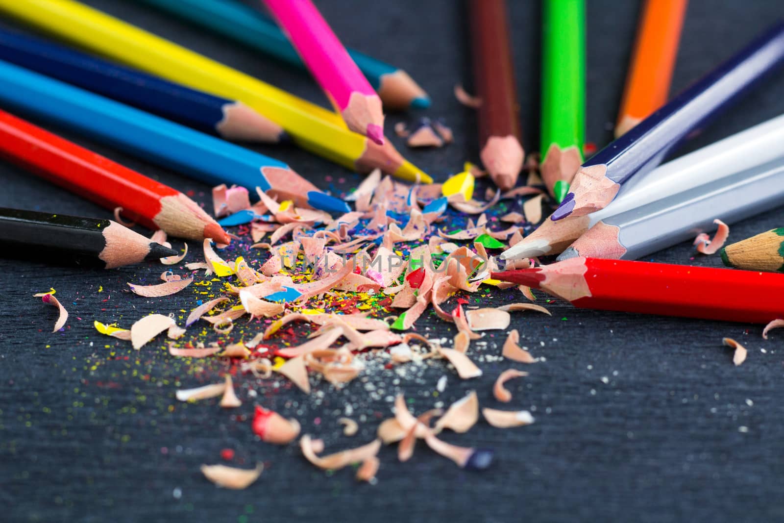 Colourful pencils with knot of wooden shavings on black surface background