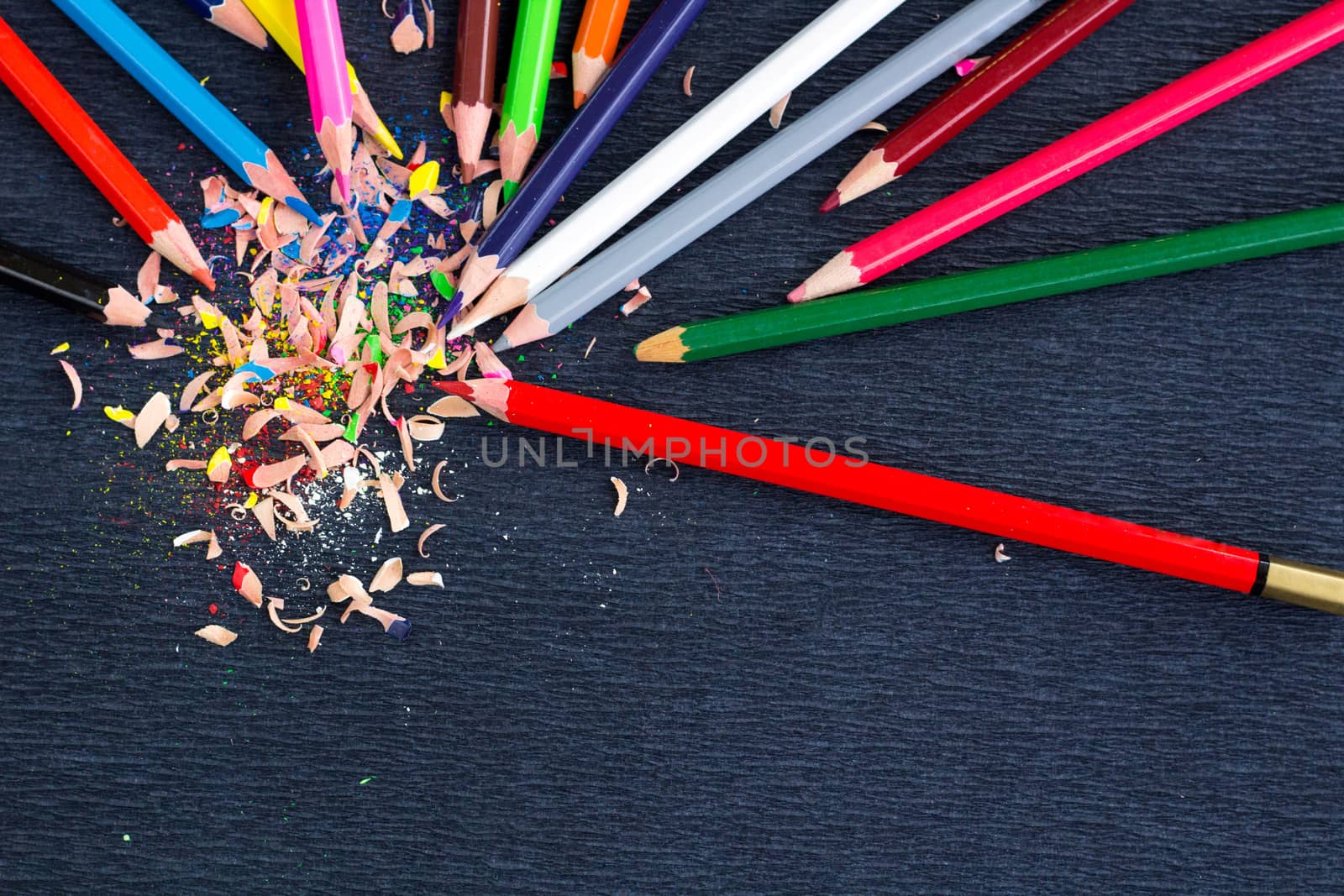 Colourful pencils with knot of wooden shavings on black surface background