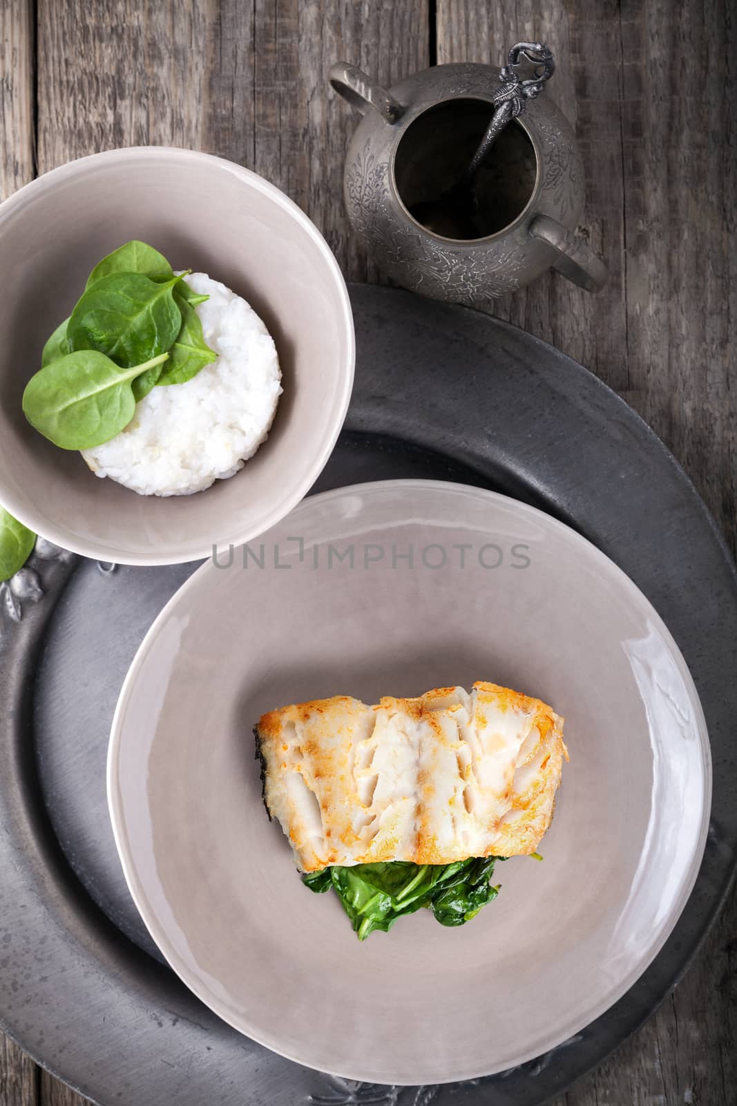 Fried cod fillets and spinach served on a wooden surface