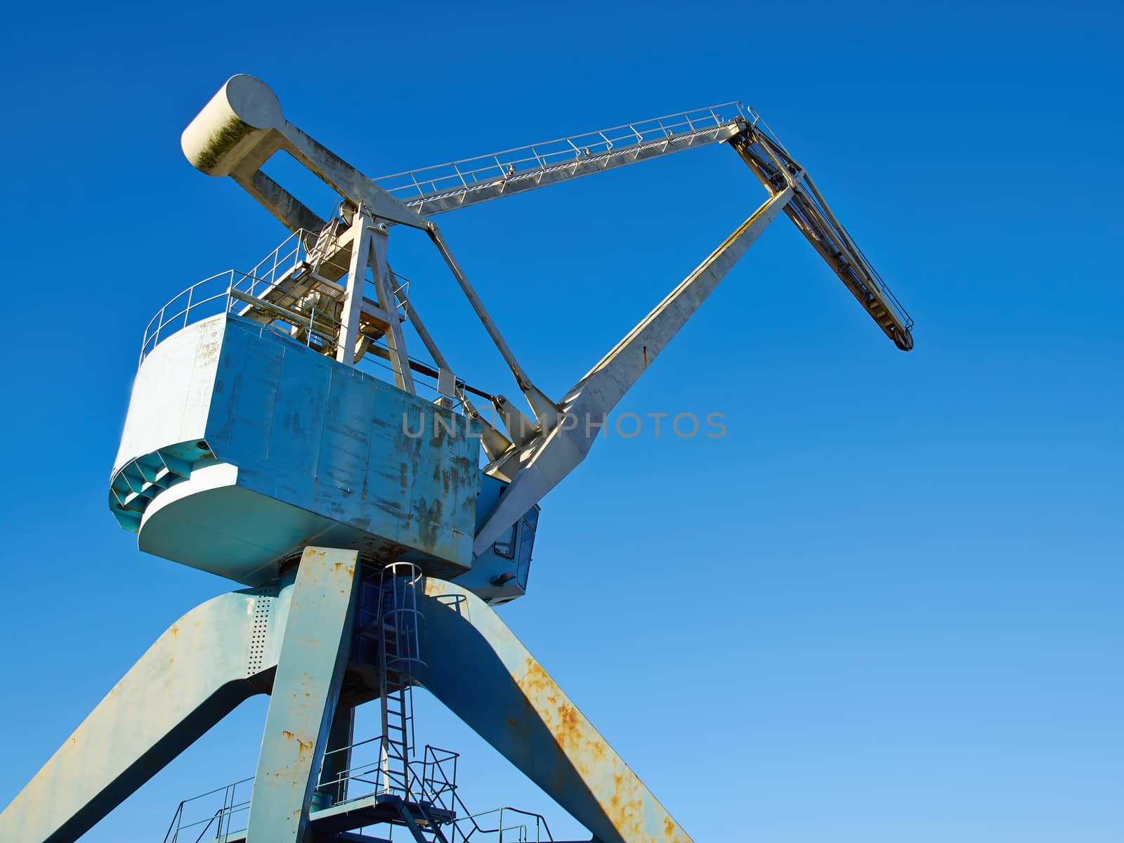 Traditional industrial metal port crane with clear blue sky background