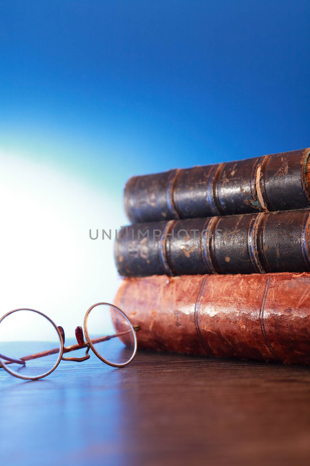 Stack of old books near spectacles on blue background with free space
