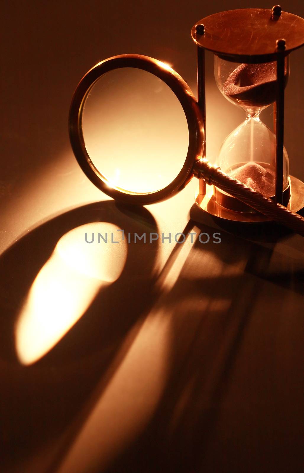 Vintage hourglass near magnifying glass on dark background with long shadow