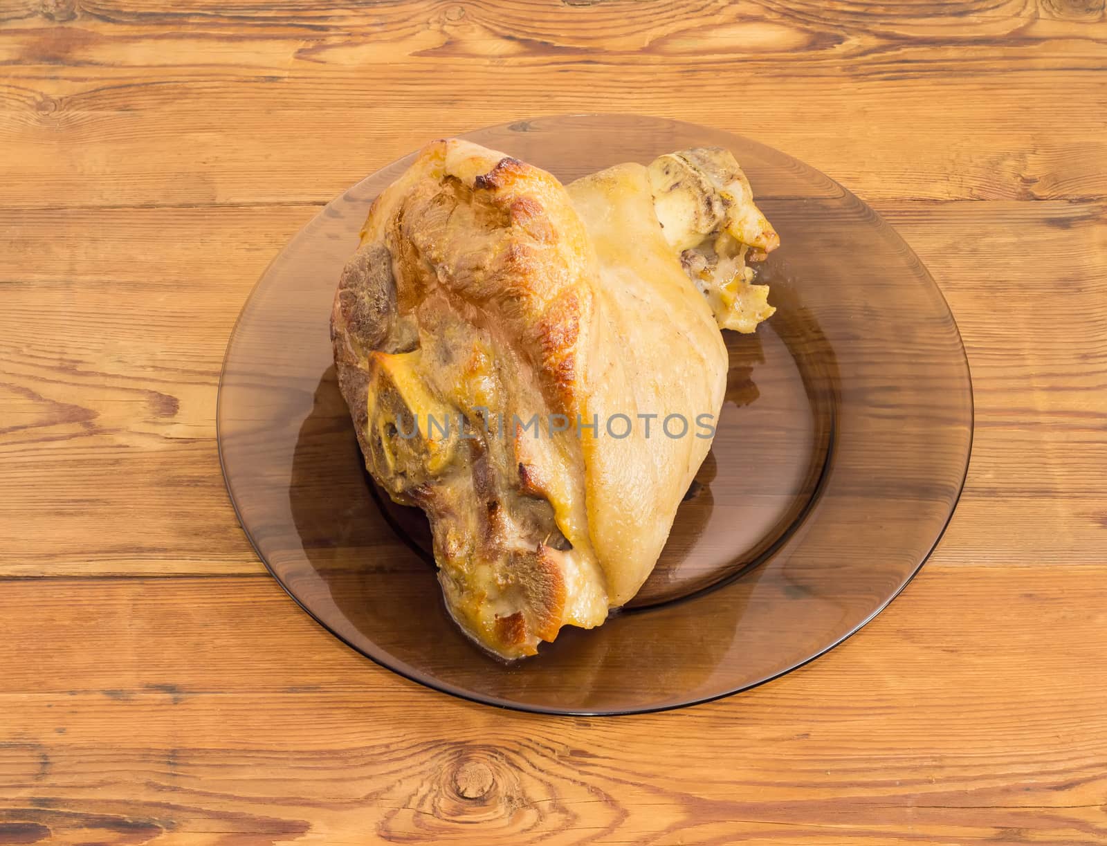 Baked ham hock on glass dish on wooden surface by anmbph