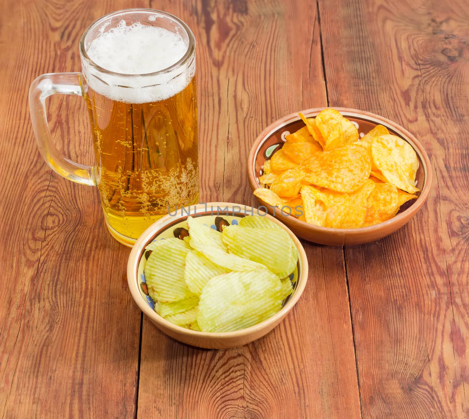 Glass tankard with lager beer, potato chip flavored paprika and wasabi in two different ceramic bowls on an old wooden planks
