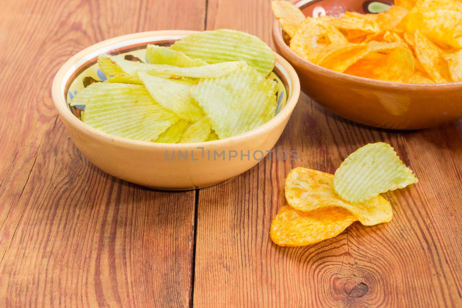 Potato chip flavored wasabi and paprika in two different ceramic bowls and separately beside closeup on an old wooden surface
