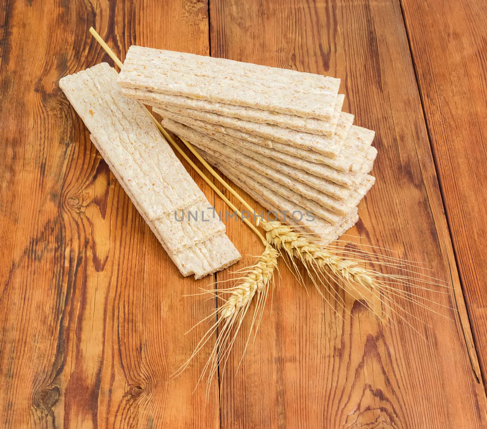 Dietary wheat wholegrain crispbread with adding a buckwheat and a barley and two wheat spikes on an old wooden surface
