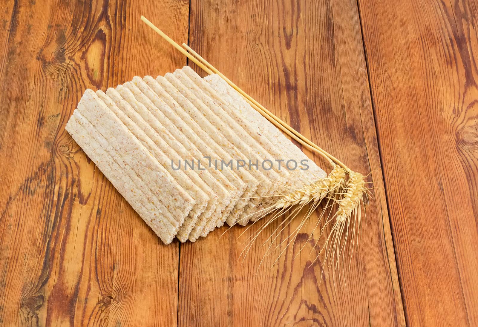 Dietary wheat wholegrain crispbread with adding a buckwheat and a barley and two wheat spikes on a surface of an old wooden planks
