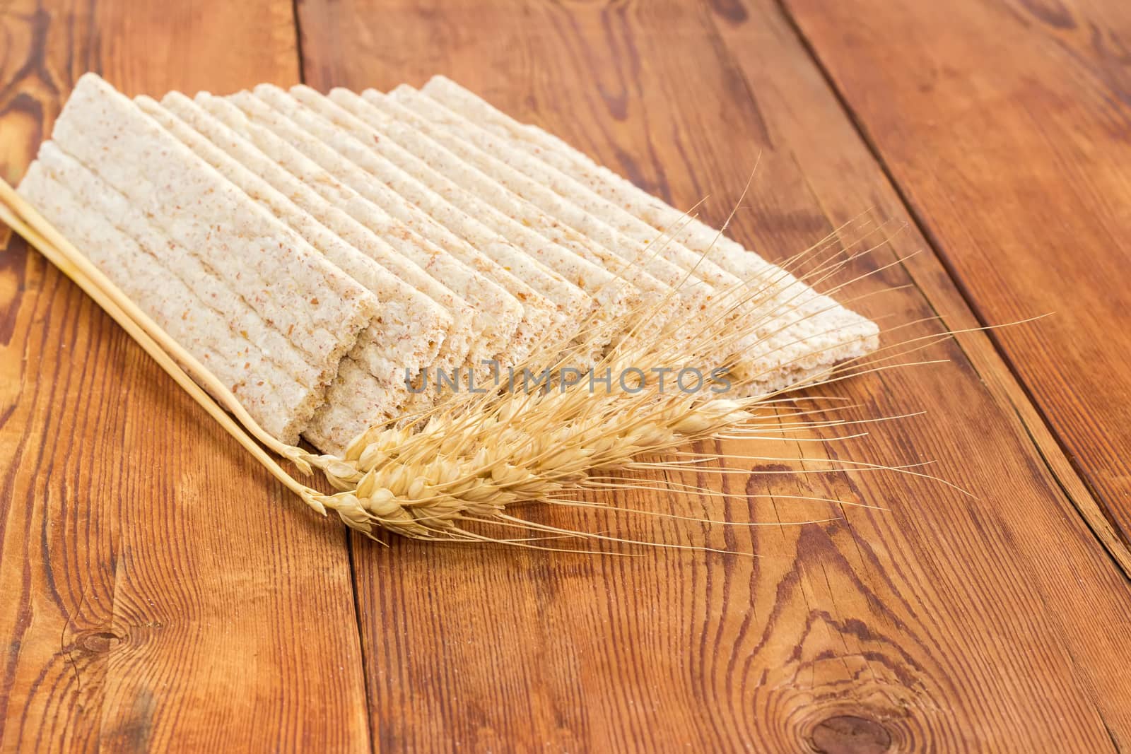 Several dietary wheat wholegrain crispbread with adding a buckwheat and a barley and two wheat spikes closeup on a surface of an old wooden planks
