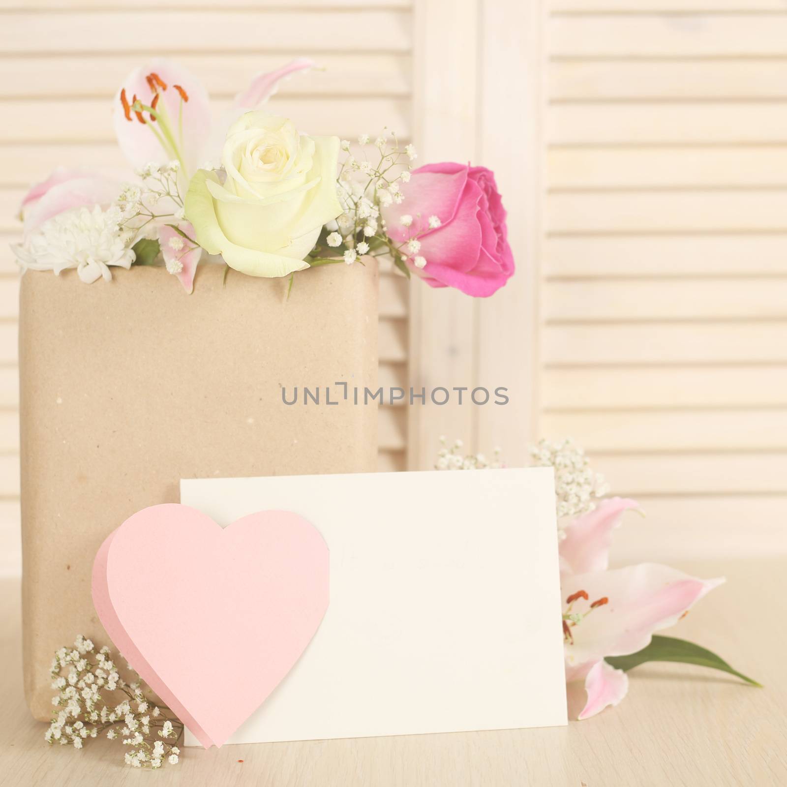 Flowers in paper bag and blank envelope on wooden background