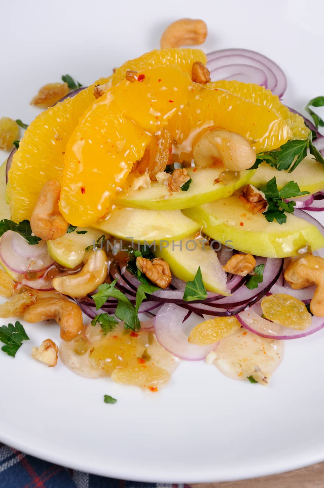 Salad with slices of orange, apple, blue onion, raisin, nuts, cashew nuts, herbs and honey sauce