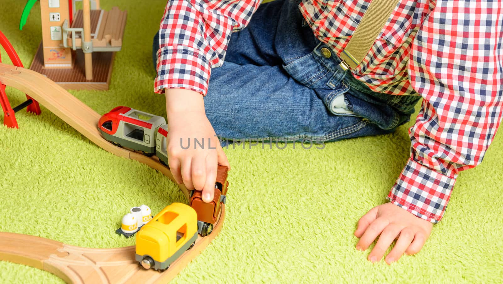 the boy plays the wooden railway sitting on a green carpet