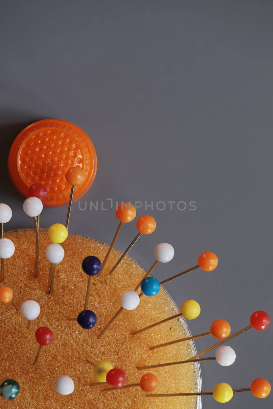 orange thimble and multicolored pins on the gray background top view macro shot