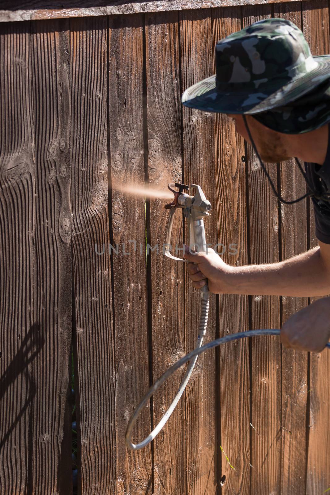 Professional Painter Spraying Yard Fence with Stain by Feverpitched