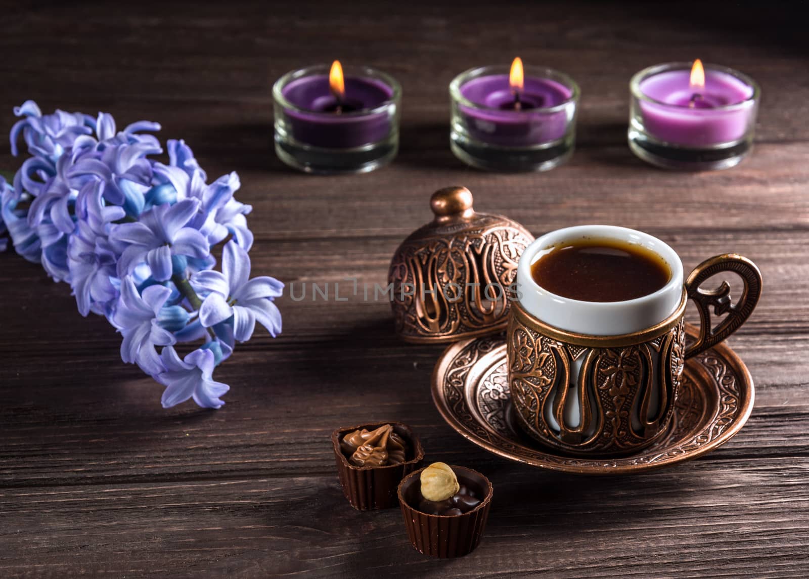 Cup of black coffee, candles and flowers on a wooden background. Dark key.