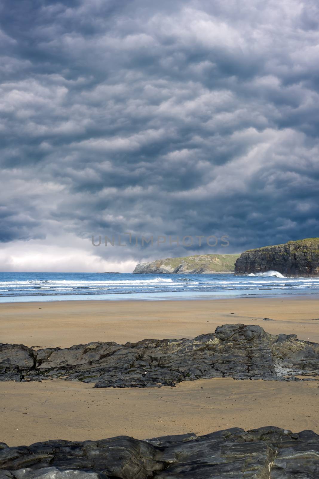 storm clouds with soft waves break on the beach and rocky sand at ballybunion