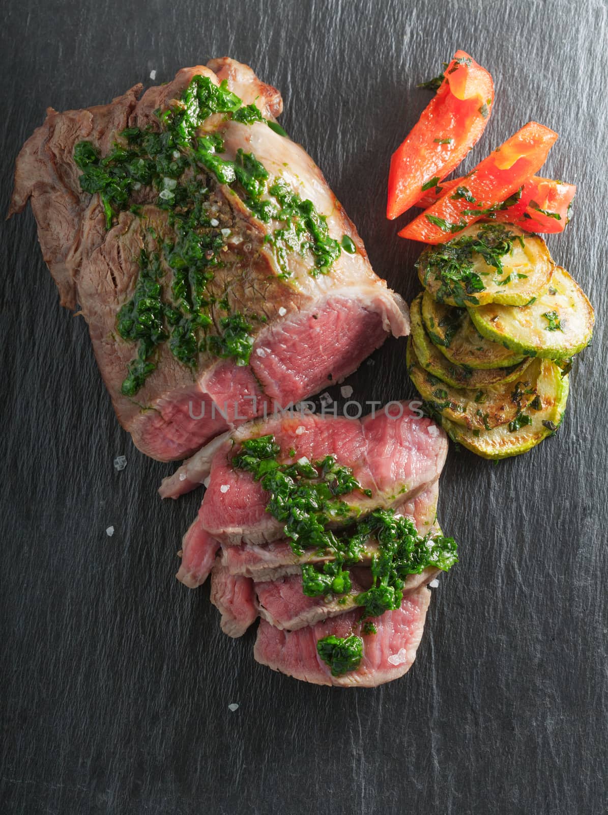 Roast Beef dinner with roasted zucchini, pepper and salsa verde on a stone plate