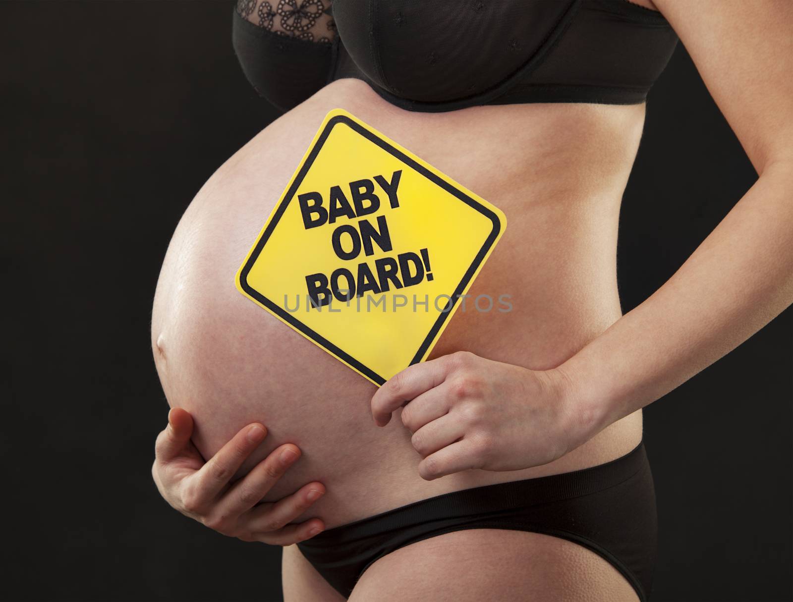 A pregnant woman abdomen close-up with a sign reading baby on board.