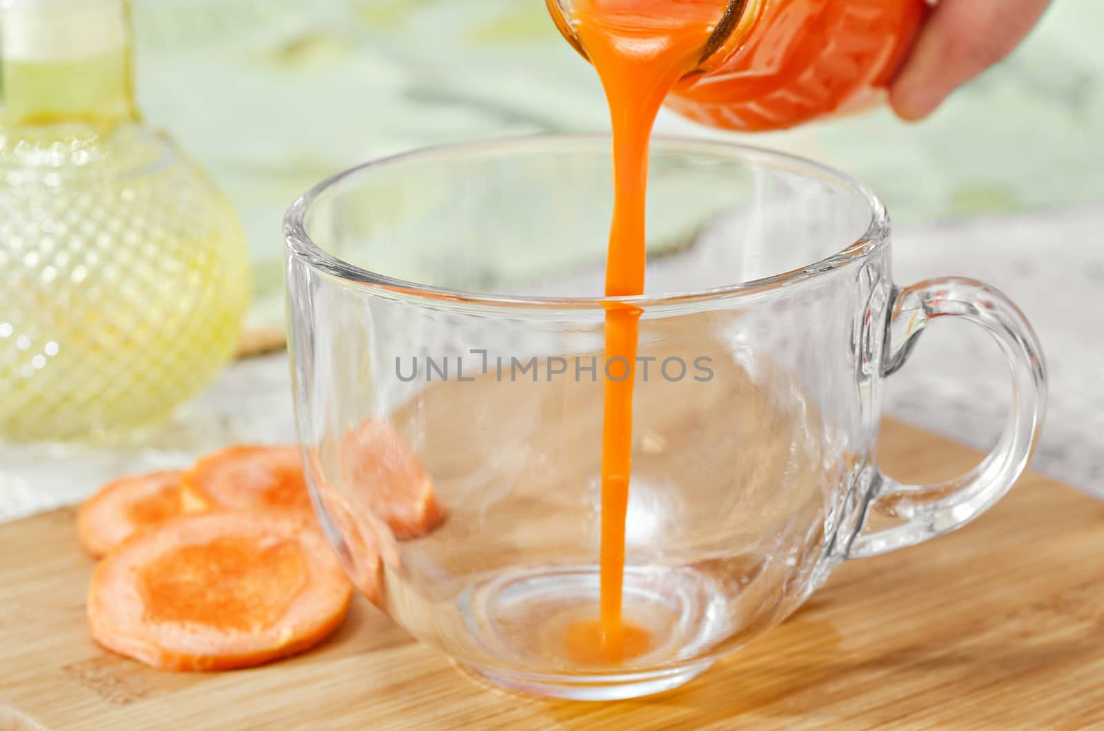 Carrot juice is poured from the bottle into an empty Cup, which stands on the table and the cutting Board, slices of carrots nearby. Selective focus.