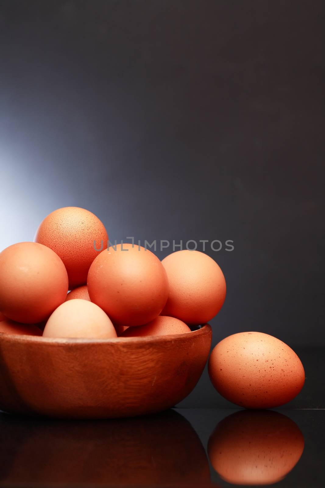 Set of raw brown eggs in wooden bowl against dark background