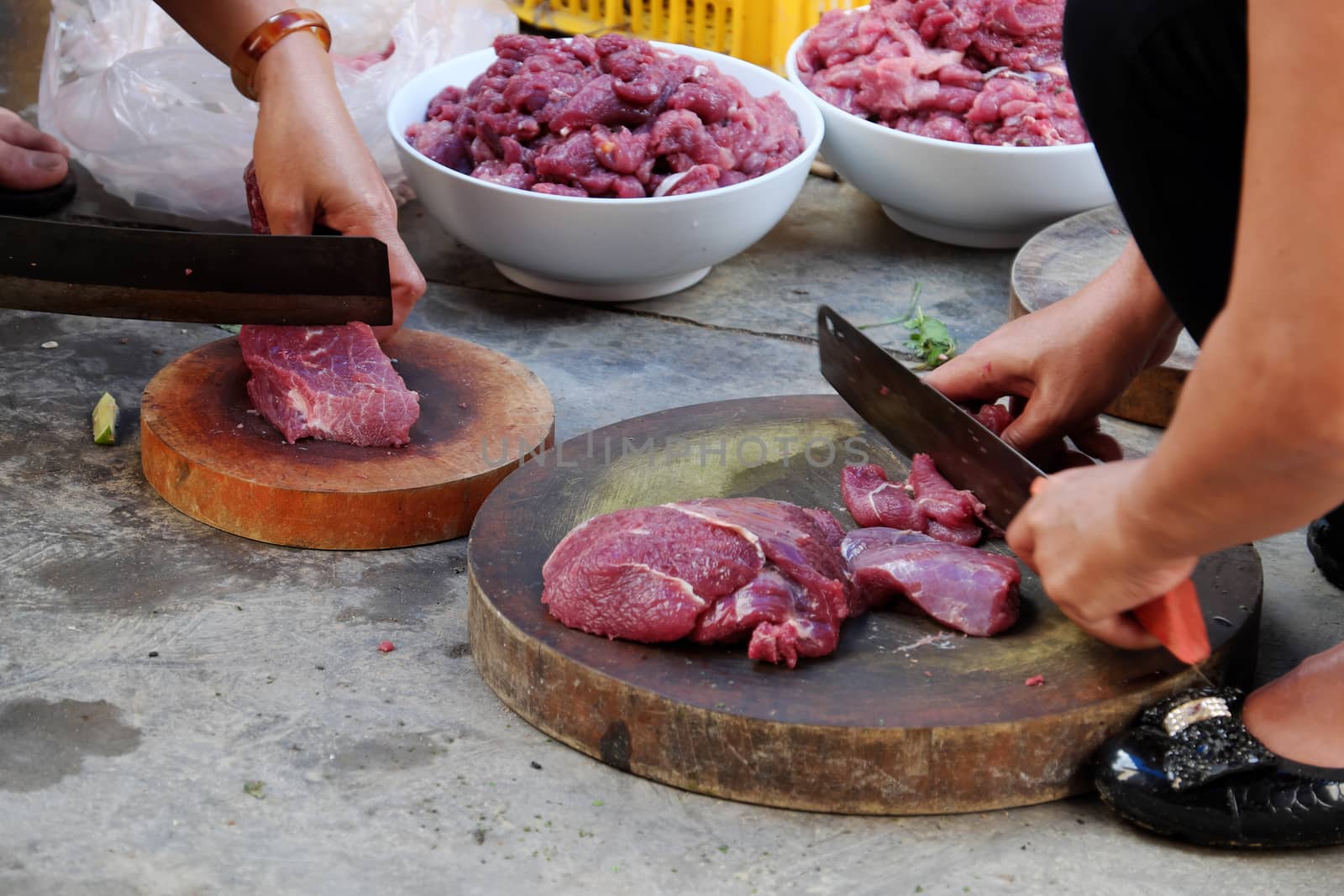 Two people cut beef meat on chopping board with food safety not good, woman sit on dirty floor and process food