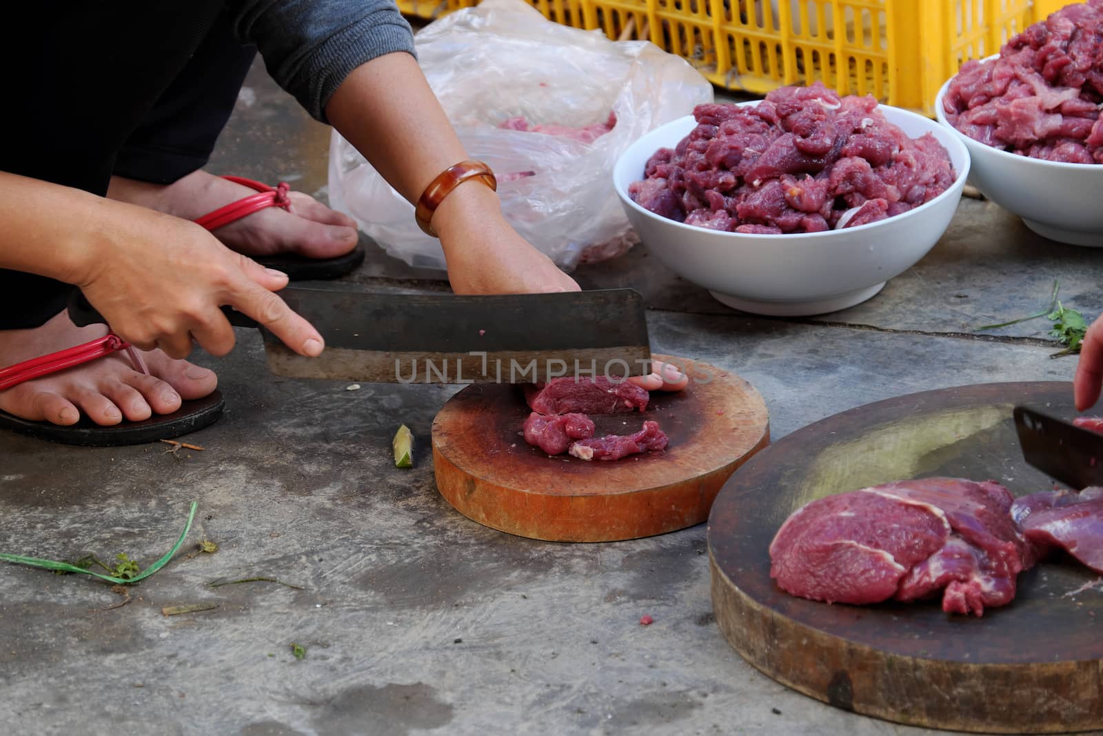 Two people cut beef meat on chopping board with food safety not good, woman sit on dirty floor and process food