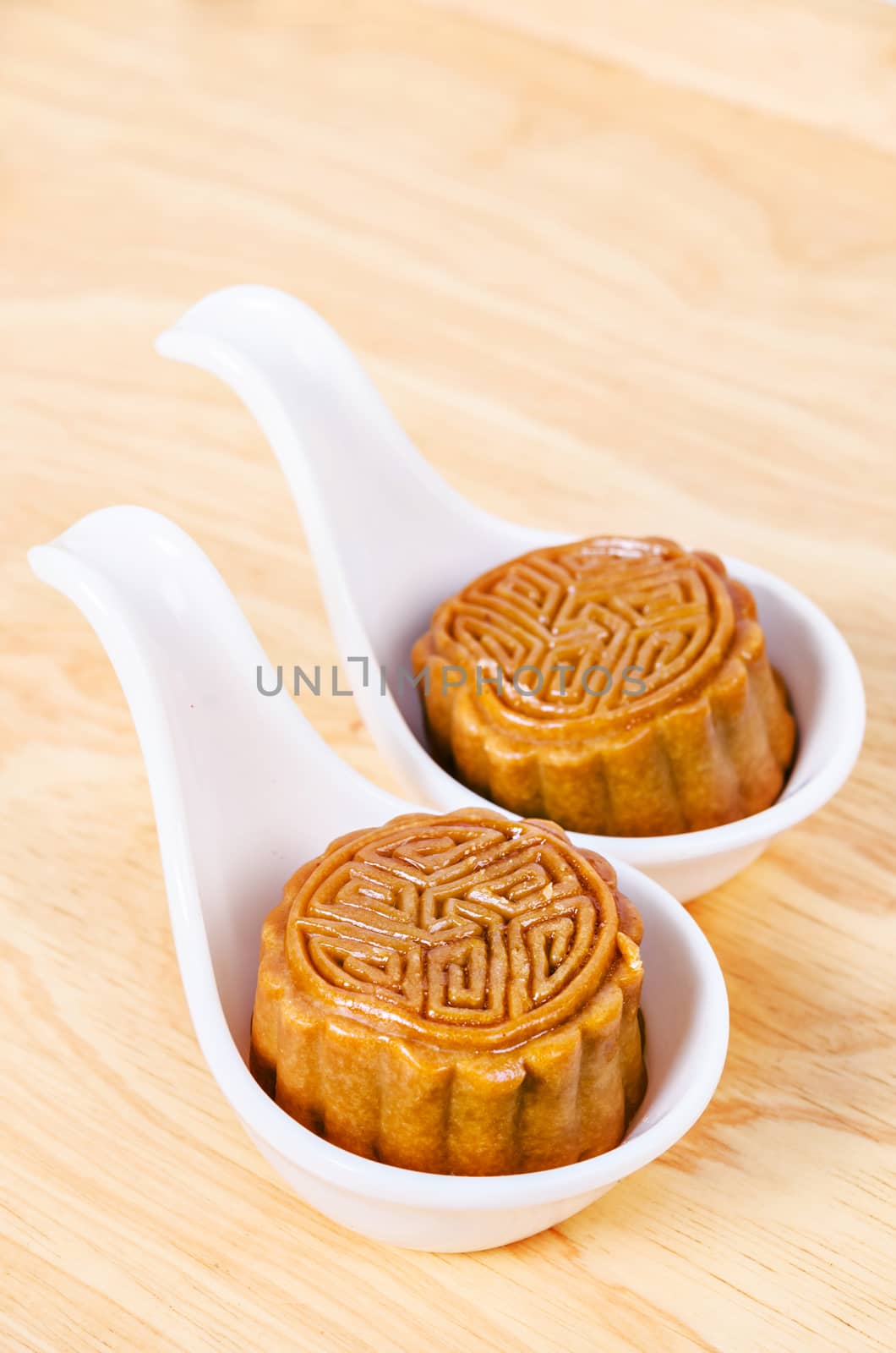 Two moon cake in white spoon on wooden background.