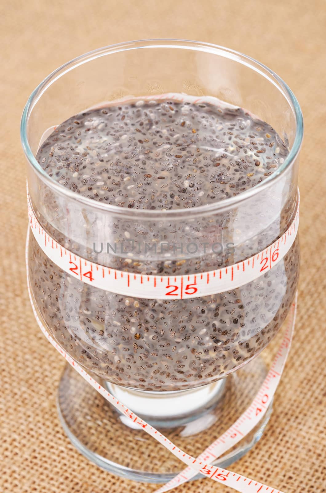 Chai seed, super food soaked in clear glass of water with and tape measure run around it on sack background.