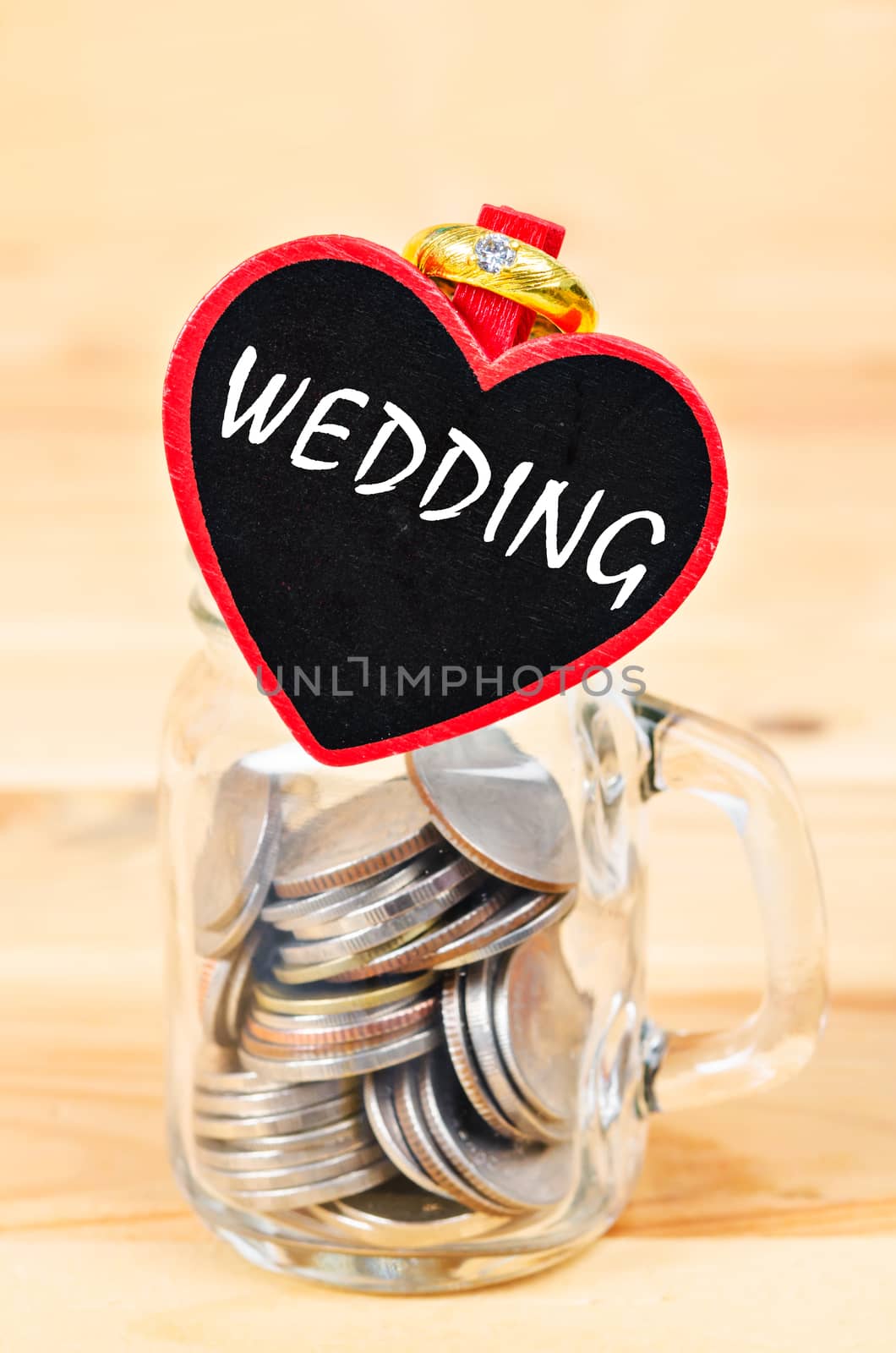 Savings in glass bank and Wedding Ring on wooden background.