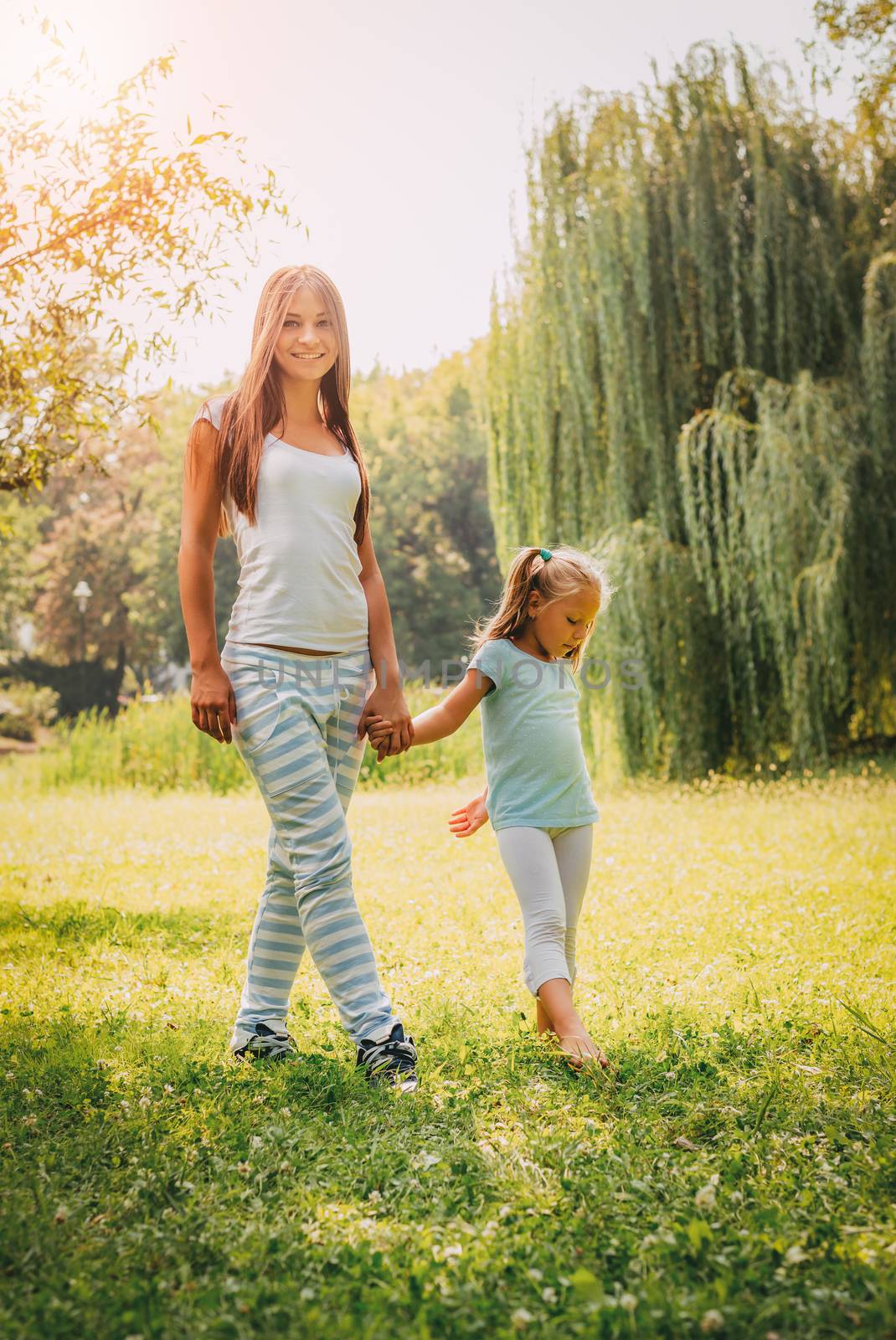 Beautiful mother and daughter walking through a park in spring day.