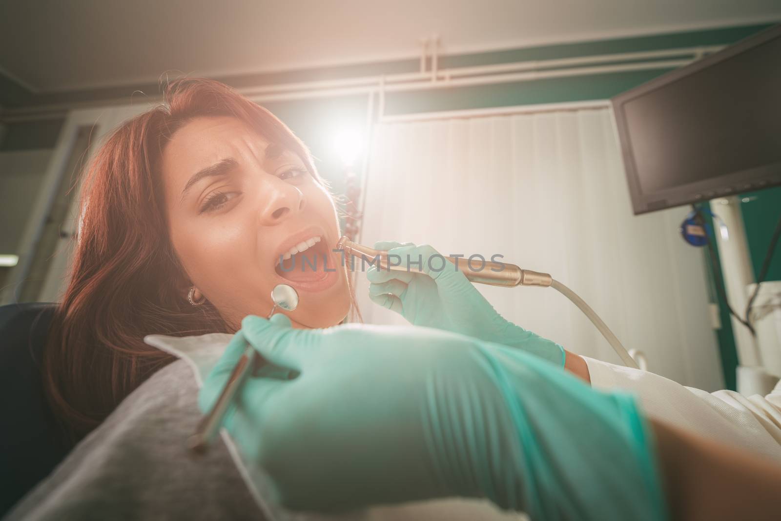 Beautiful young woman in visit at the dentist office. She is sitting on a chair and dentist repair teeth on her. Selective focus. 