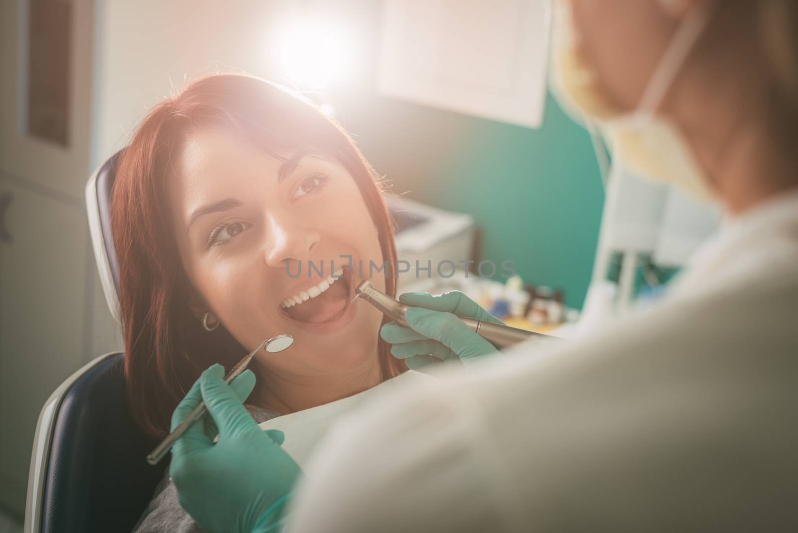 Beautiful young woman in visit at the dentist office. She is sitting on a chair and dentist repair teeth on her. Selective focus. 