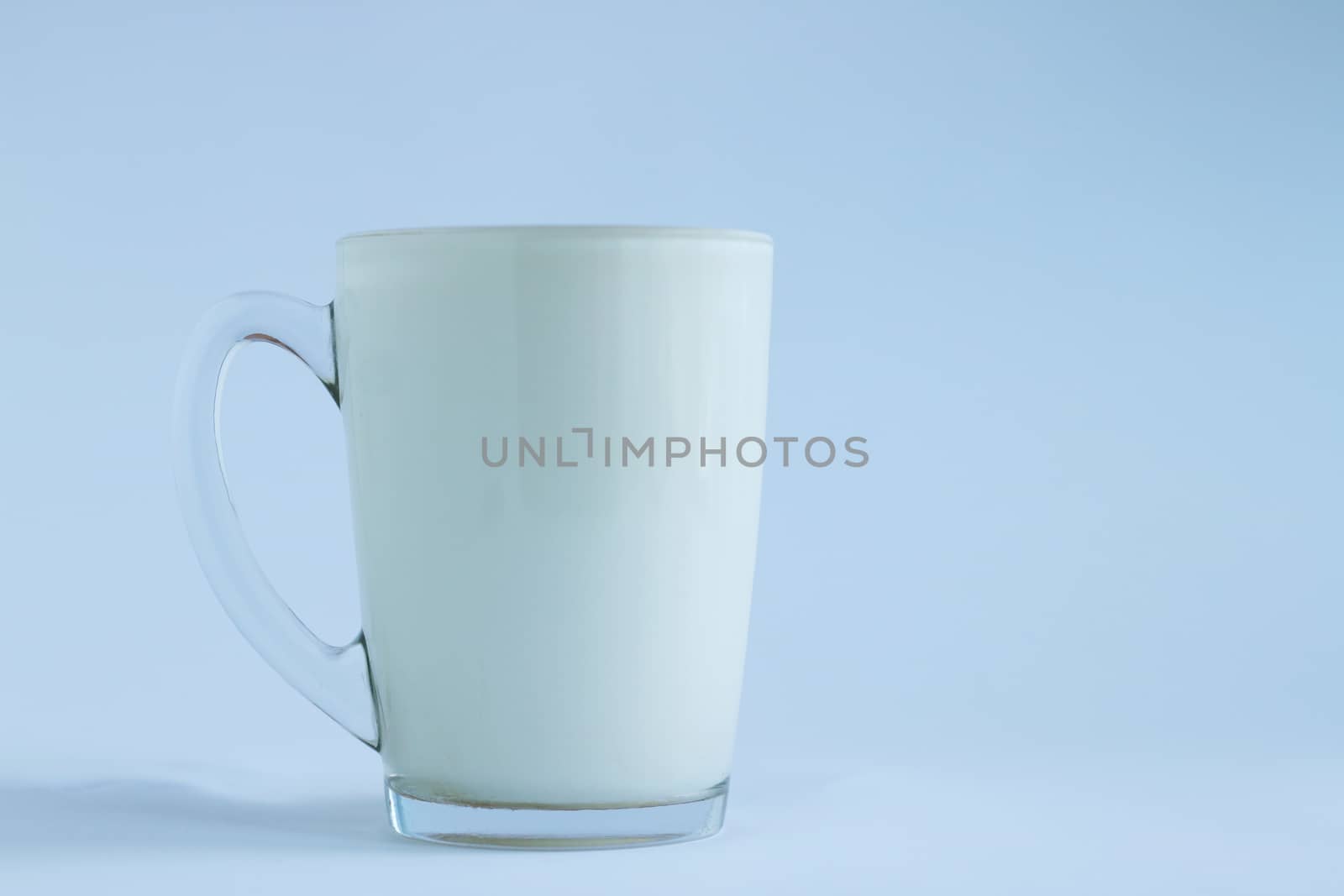 Full transparent glass poured milk on light white and blue background