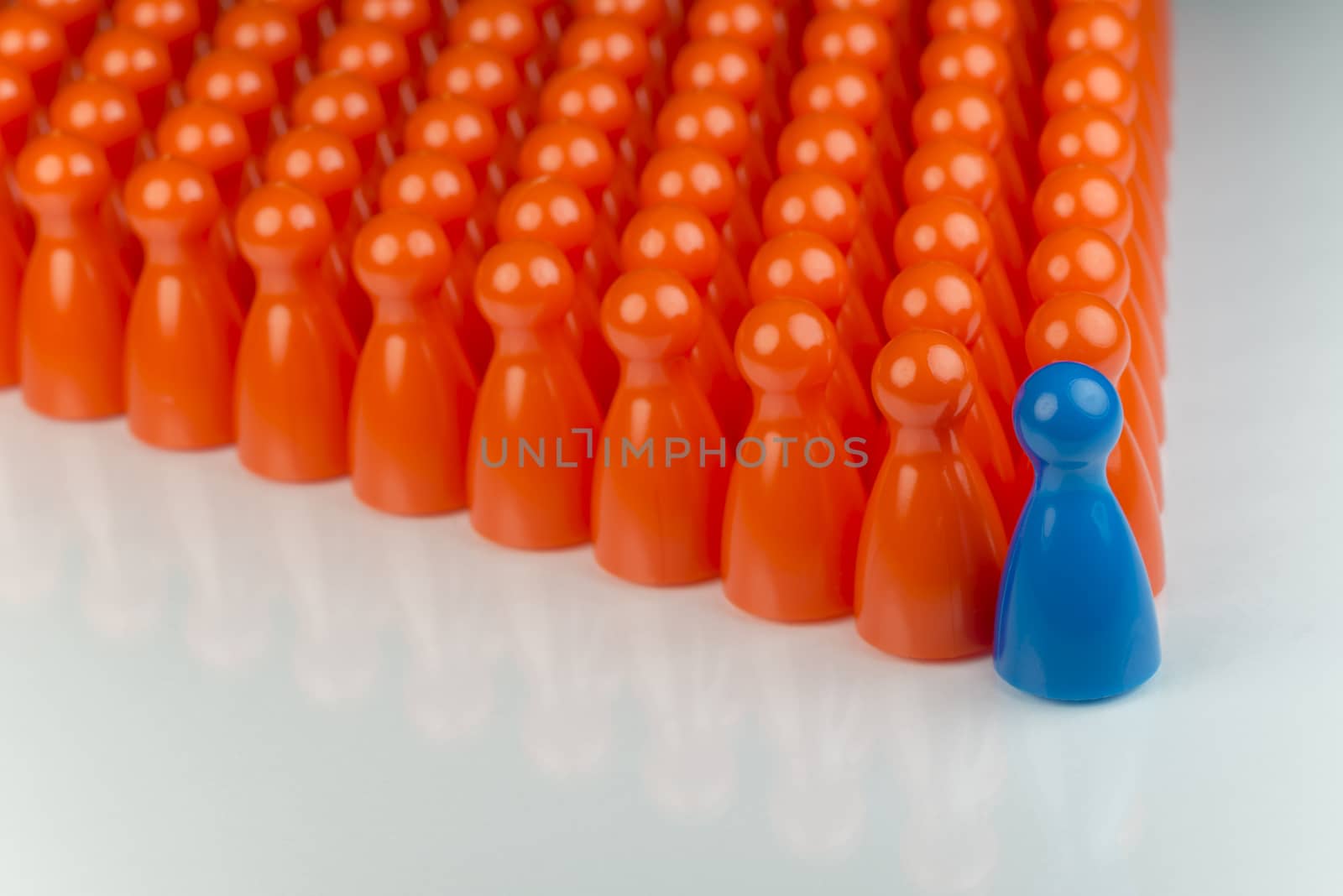 Conceptual orange game pawns and a blue play pawn as abstract display of inequality in color and number of
