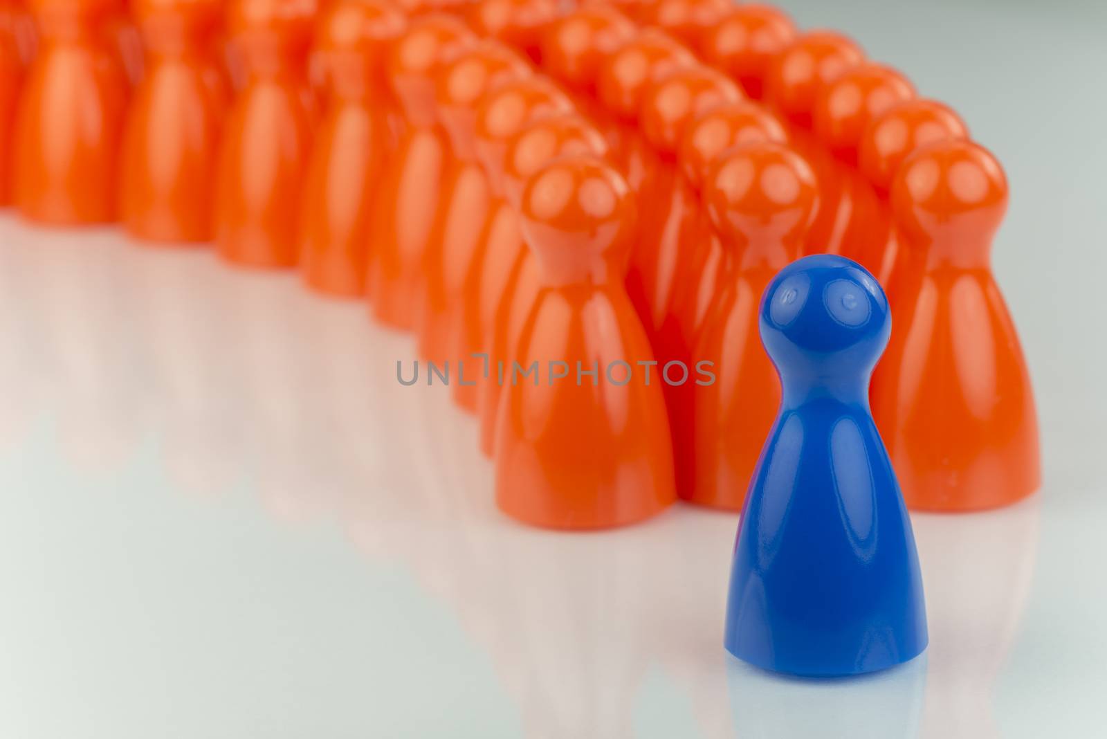 Conceptual orange game pawns and a blue play pawn as abstract display of inequality in color and number of
