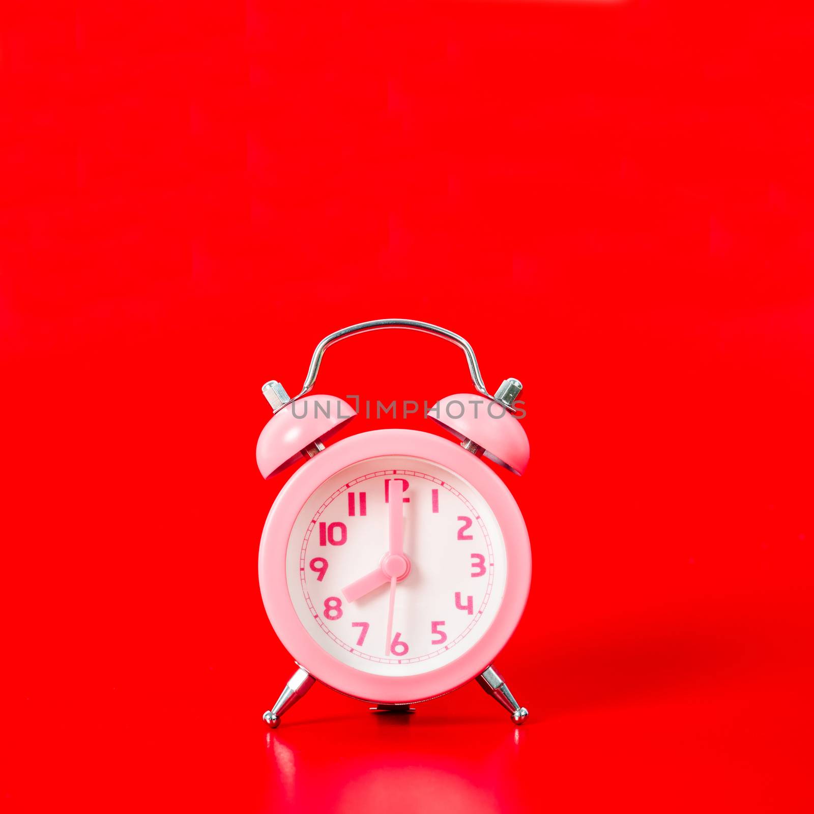 Pink alarm clock with shadow on red background.