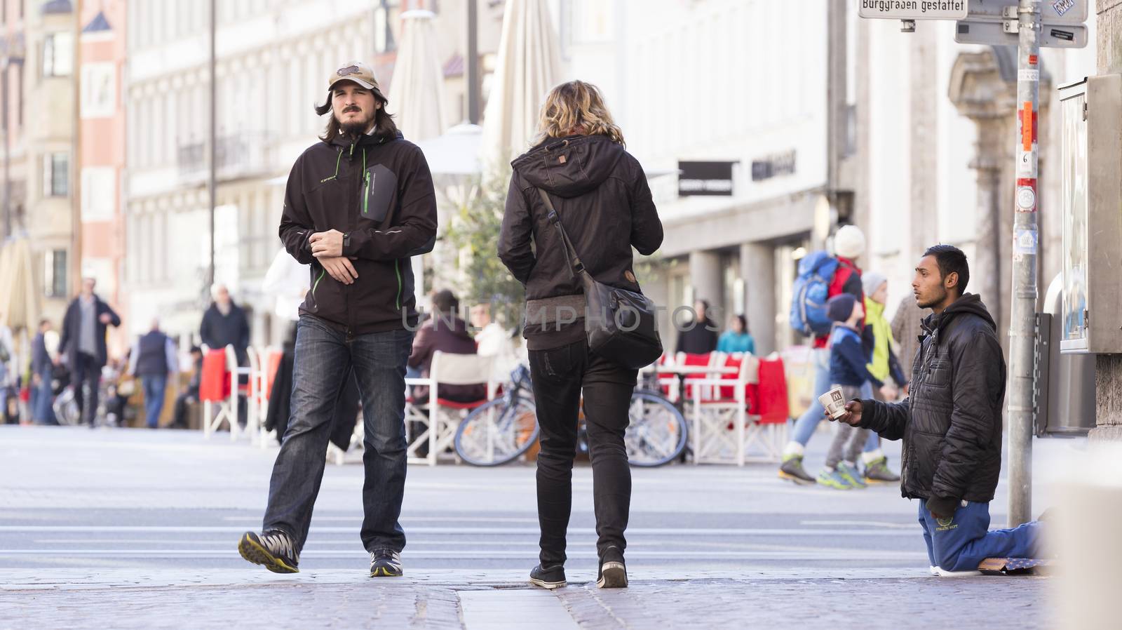 INNSBRUCK, AUSTRIA – NOVEMBER 1st 2015: Refugee begging for help in the streets of Innsbruck with people walking by.