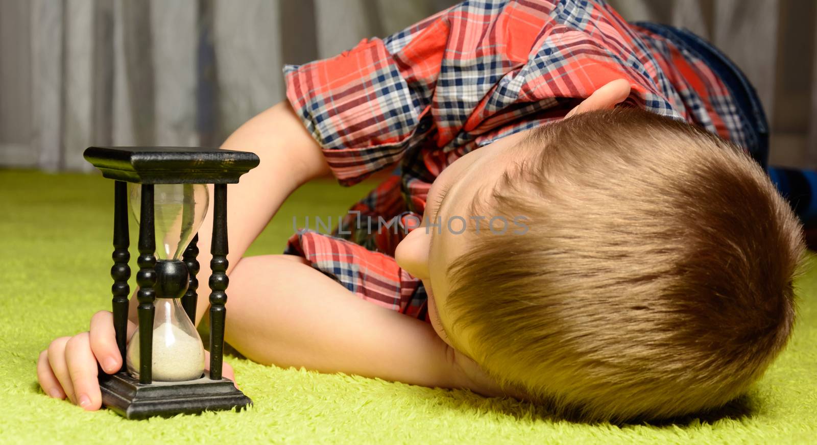 little boy lying on the floor and looking at hourglass