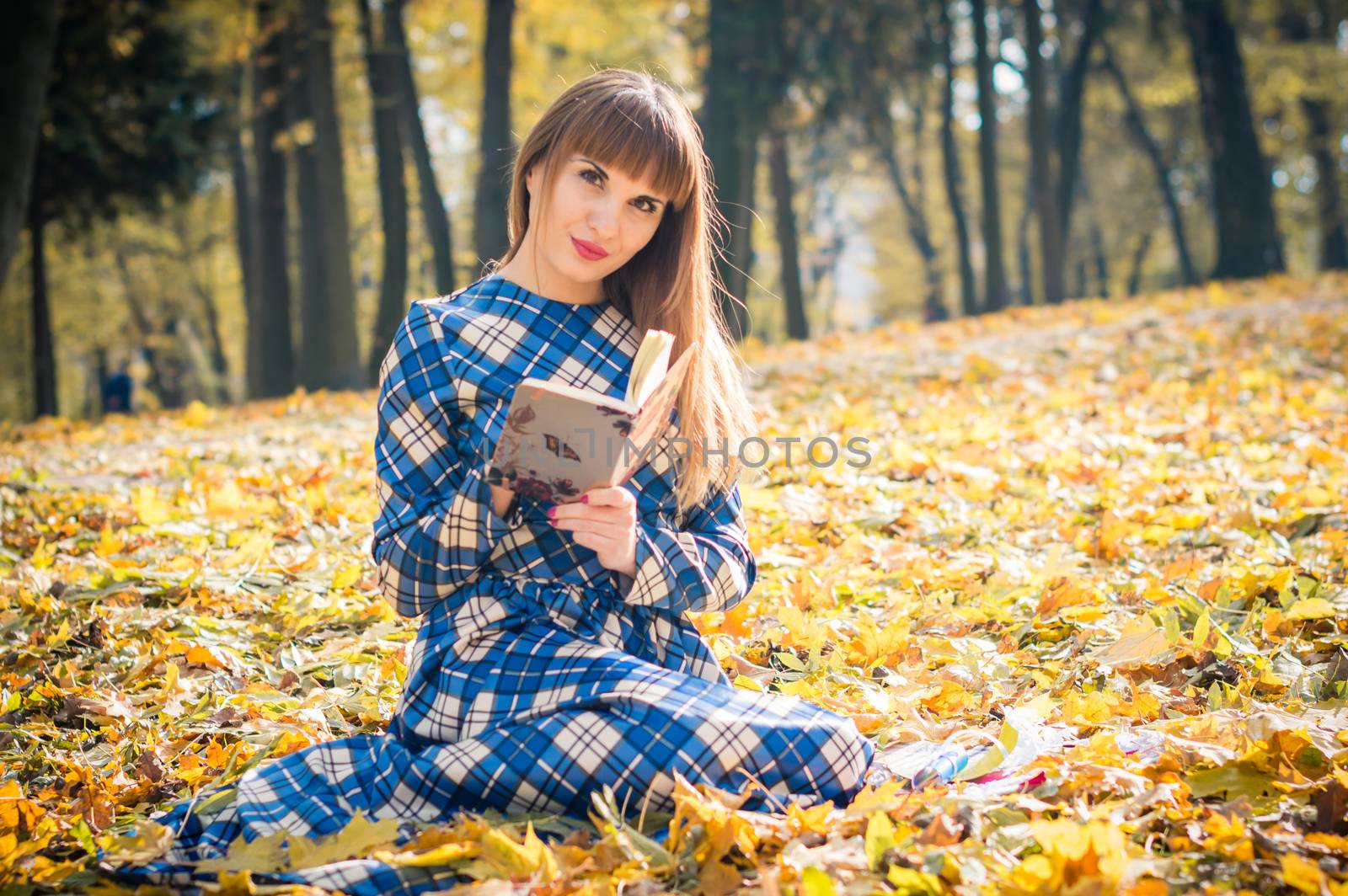 beautiful girl with long straight hair in a blue long dress reading a book in the autumn park