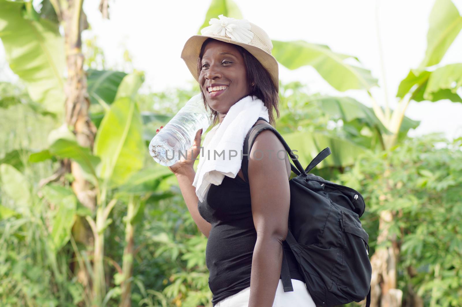 This smiling young woman holding a bottle of mineral water, carrying a bag  on her on her back returned to town afteralatesportif training