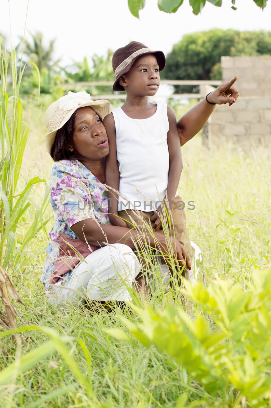 This young woman squatting shows something to her child in the bush.