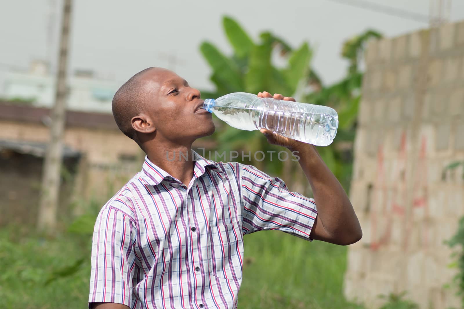 This young  man is trying to quench hiq thirsty with a large bottle of mineral water.
