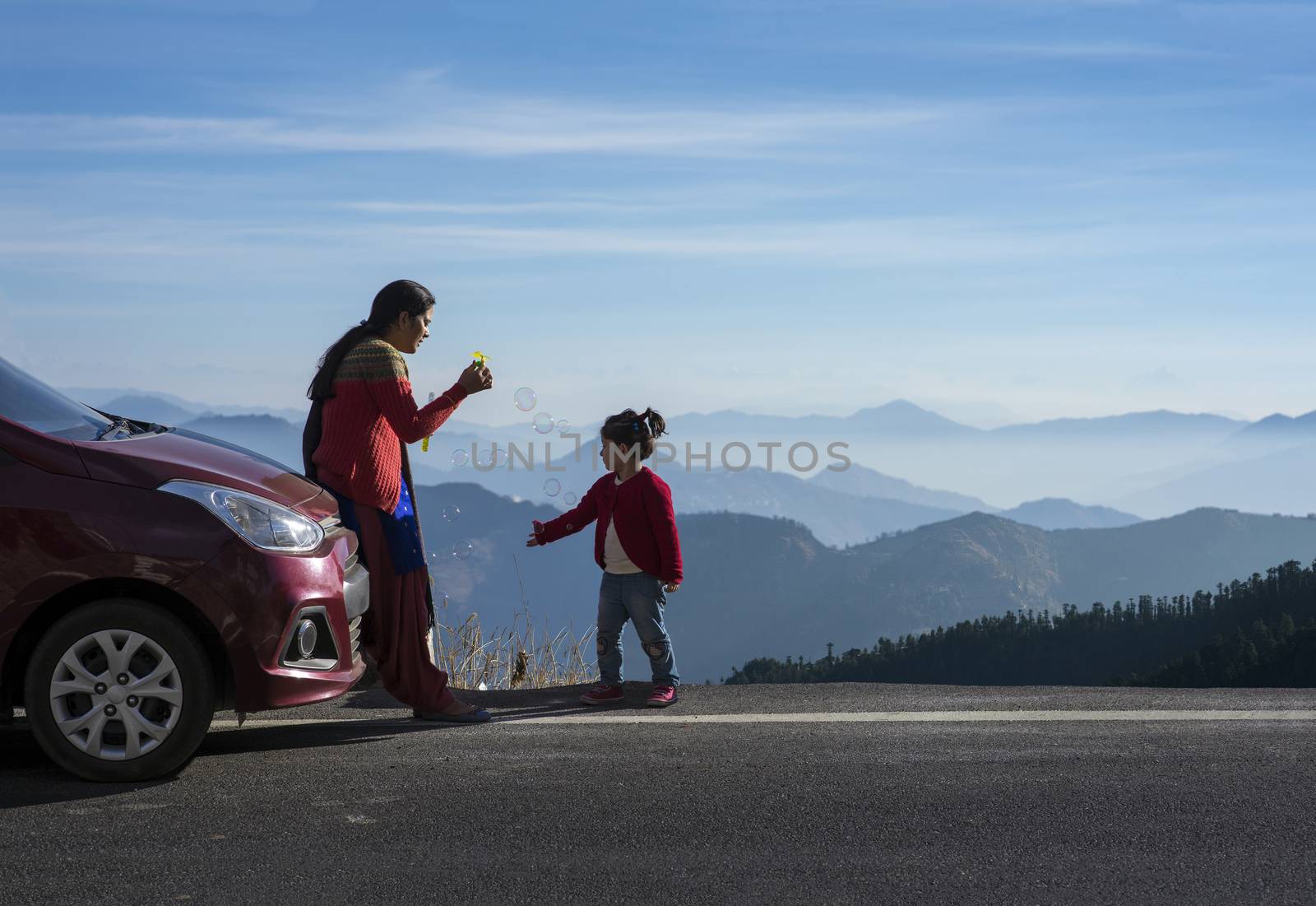 Mother and daughter enjoying the road trip and winter vacation in Shimla, Himachal Pradesh, India. Car travel vacation concept photo against Himalayan mountain in the background.