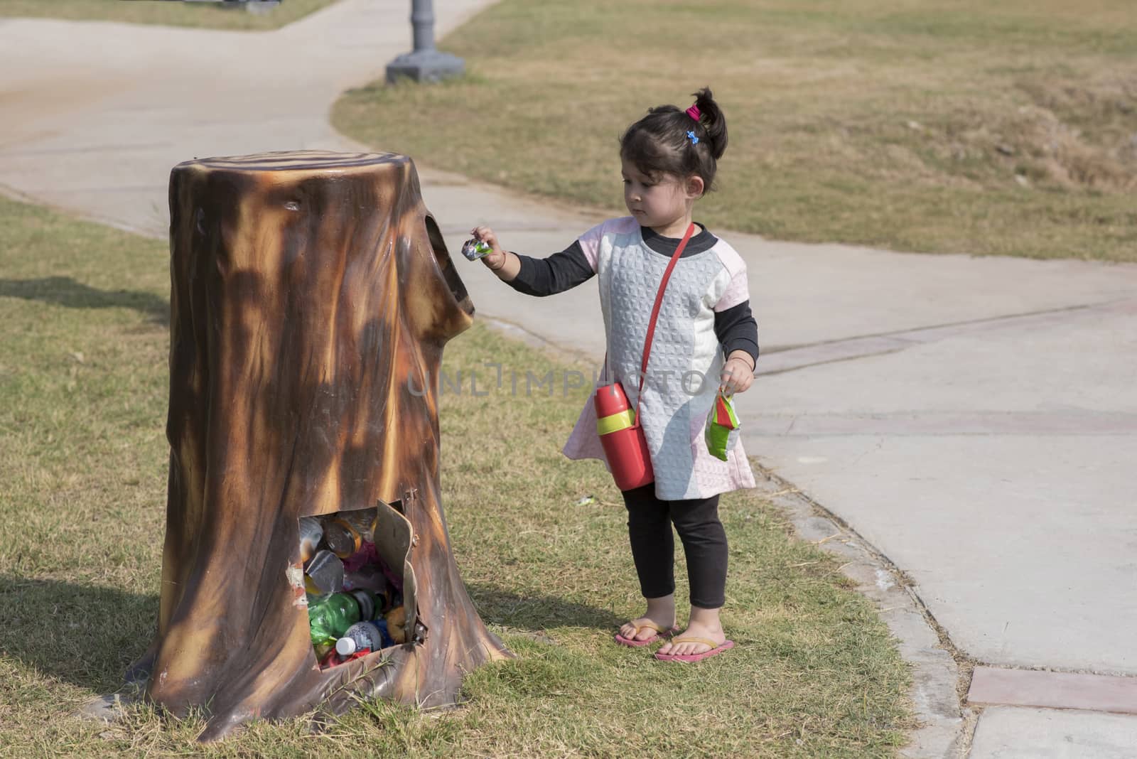 Cute little girl putting waste in the bin outdoor in a park.