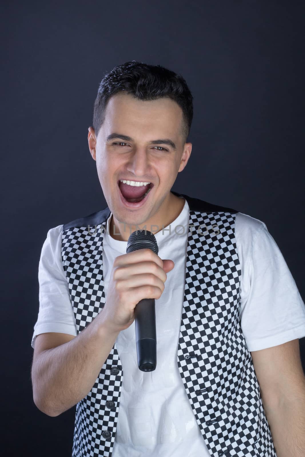 Young black-haired man dressed in black and white performs singing to microphone