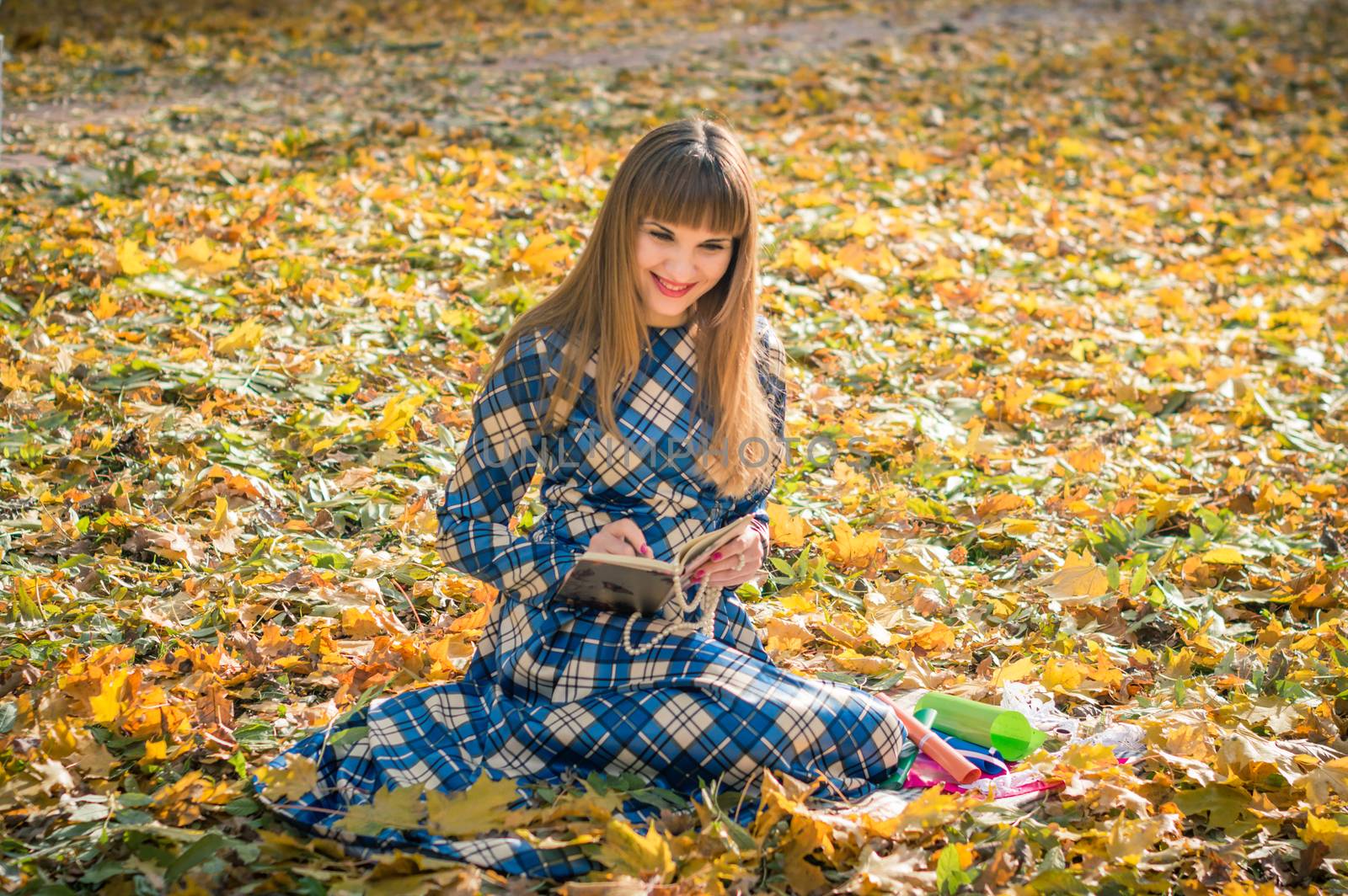 beautiful girl with long straight hair in a blue long dress reading a book in the autumn park