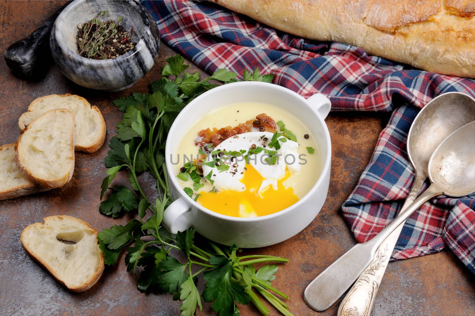 Garlic potato cream soup with bacon and poached eggs, herbs, spices
