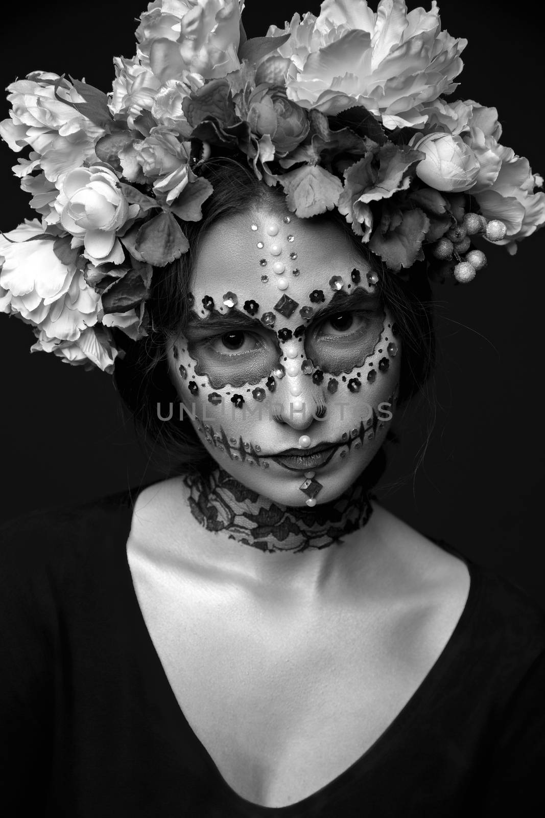 Fashion black and white portrait of a beautiful Halloween model with creative make up,  rhinestones and wreath of flowers on black background