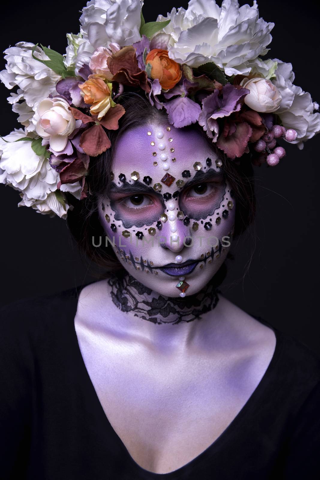 Fashion portrait of a beautiful Halloween model with creative make up,  rhinestones and wreath of flowers on black background