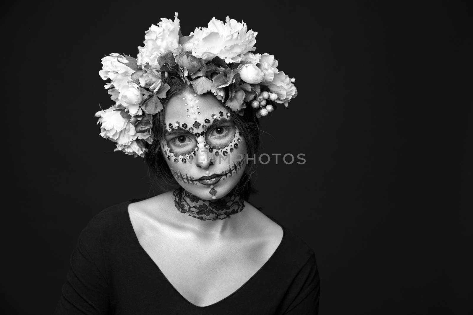 Creative black and white portrait of a beautiful Halloween model with creative make up,  rhinestones and wreath of flowers on black background